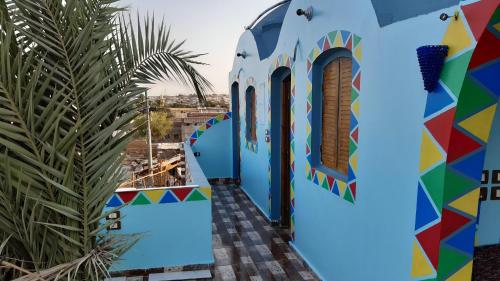 a colorful building with a palm tree in the foreground at NeNeKaTo Nubian House in Aswan