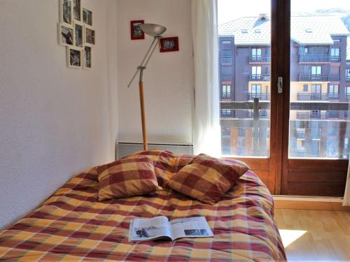 a bed with a book and a lamp and a window at Appartement rénové 2 étoiles, pied de pistes, balcon sud, casier à ski - FR-1-330-218 in Risoul