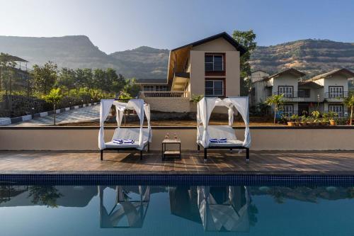 two chairs and a table next to a swimming pool at Asanjo Villa by VEO - Part of StayVista in Mulshi