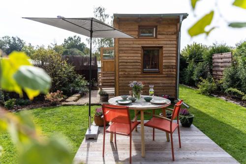 una mesa y sillas bajo una sombrilla en un jardín en Zirbenholz Tiny House "Waldhauszeit" am See, en Mücke