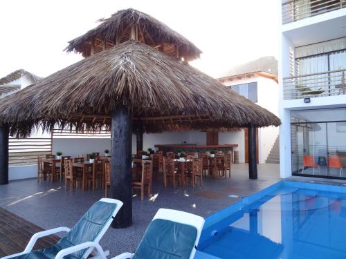 a restaurant with a straw umbrella and chairs and a pool at Akas Hotel Apartamentos in Canoas De Punta Sal