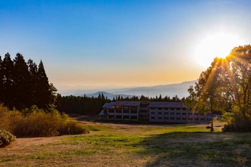 a building in a field with the sun setting in the background at Kyukamura Myoko in Myoko