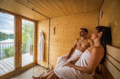 Ein Mann und eine Frau sitzen in einer Sauna in der Unterkunft Chalet Resort Seenland in Steinberg