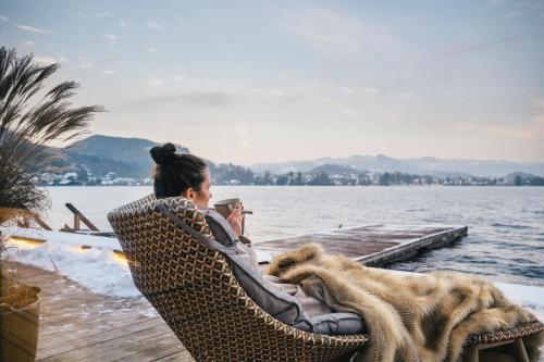 a woman sitting in a chair next to the water at Das Traunsee - Das Hotel zum See 4 Stern Superior in Traunkirchen