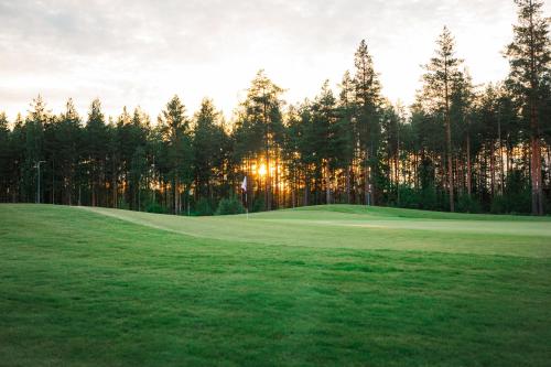 un campo de golf con la puesta de sol detrás de los árboles en Holiday Club Saimaa Apartments en Imatra