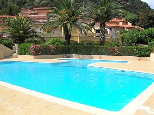 une grande piscine bleue avec des palmiers et un bâtiment dans l'établissement Appartement 3 pièces 6 pers avec terrasse, clim, piscine privée, parking - FR-1-251-81, au Lavandou