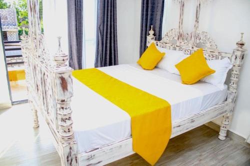 a white bed with yellow pillows in a room at Shany’s Villa 3bdrm with private swimming pool in Mombasa