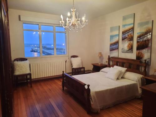 a bedroom with a bed and two chairs and a chandelier at Apartamentos Puerto de Aguiño in Couso