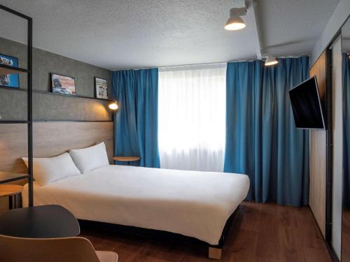 een slaapkamer met een groot wit bed en blauwe gordijnen bij ibis Orléans Nord Saran in Saran