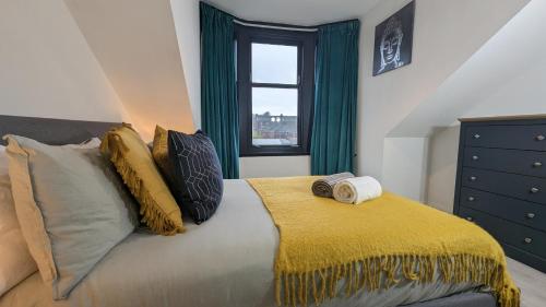 a bedroom with a bed with a yellow blanket and a window at Lovely 2 Bedroom Apartment in Central Location in Greenock