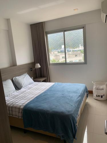 ein Schlafzimmer mit einem Bett mit einer blauen Decke und einem Fenster in der Unterkunft Flat moderno e sofisticado in Rio de Janeiro