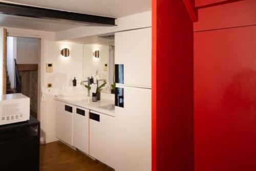 une cuisine avec des placards blancs et un mur rouge dans l'établissement Haut MaraisJolie duplex 33m2…, à Paris