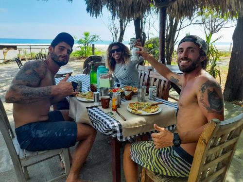 Popoyo Surfcamp في بوبويو: مجموعة من ثلاثة رجال يجلسون على طاولة يأكلون الطعام
