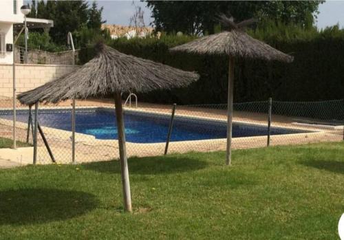 two straw umbrellas in the grass near a pool at Dúplex con espectaculares vistas del Rompido in El Rompido