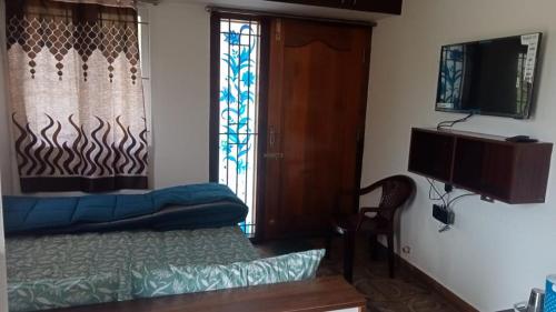 Cette chambre comprend un lit, une télévision et une fenêtre. dans l'établissement Harini Nivas, à Kodaikānāl