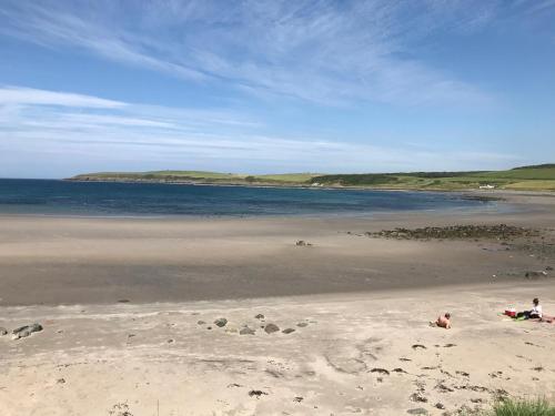 a beach with people sitting on the sand and the water at Curlew Cottage and Sunset View 