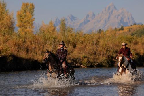two people are riding horses through the water at Heart Six Ranch in Moran