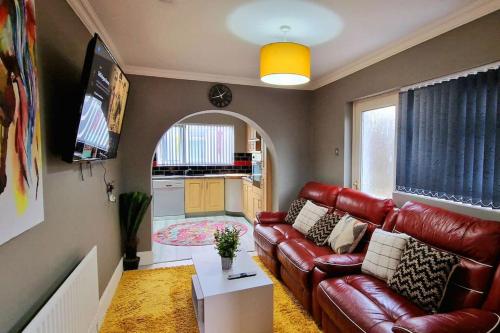 a living room with a red leather couch and a kitchen at 4 bedroom House Coventry Sleep 9 + 3Parking spaces in Coundon