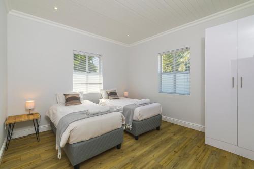 Habitación con 2 camas, paredes blancas y suelo de madera. en Irene Avenue Apartment - With backup Electricity!, en Somerset West