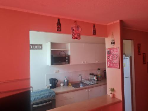 a kitchen with red walls and a sink and a refrigerator at Hermoso departamento en condominio privado, cercano a playas y centros comerciales in El Tabo