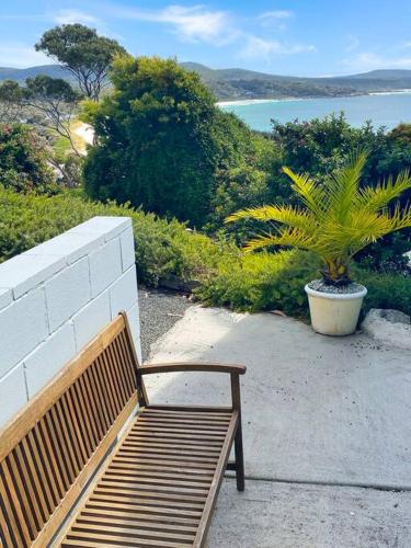 a wooden bench sitting next to a wall with a plant at Bella Cottage - Bay of Fires Beach House in Binalong Bay