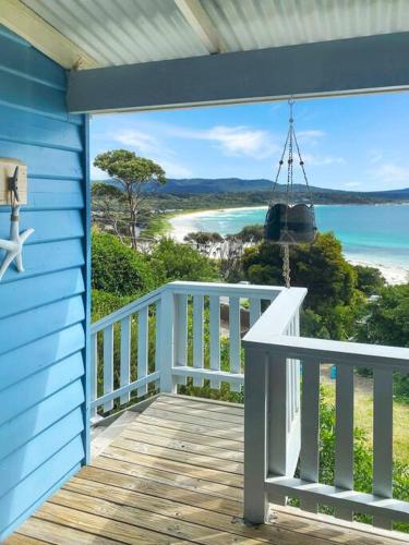 a blue house with a balcony with a view of the ocean at Bella Cottage - Bay of Fires Beach House in Binalong Bay