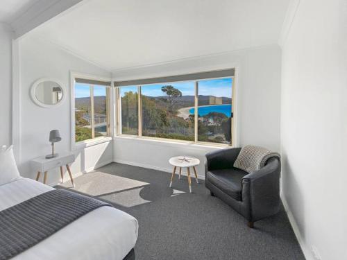 a bedroom with a bed and a chair and a window at Bella Costa - Bay of Fires Beach House in Binalong Bay