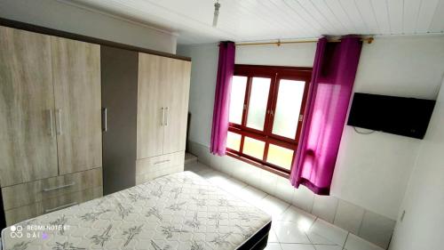 1 dormitorio con 1 cama y una ventana con cortinas rosas en Residencial família Milani 30 metros do mar Torres, en Torres