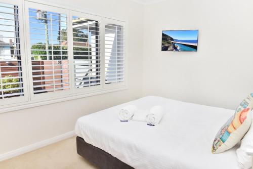 a bedroom with a bed with white sheets and windows at Point Bulli in Bulli