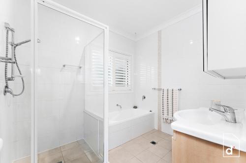 a white bathroom with a shower and a sink at Point Bulli in Bulli