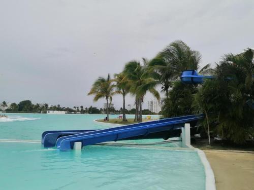 a blue water slide in a pool with palm trees at Playa Blanca Apartamentos in Río Hato