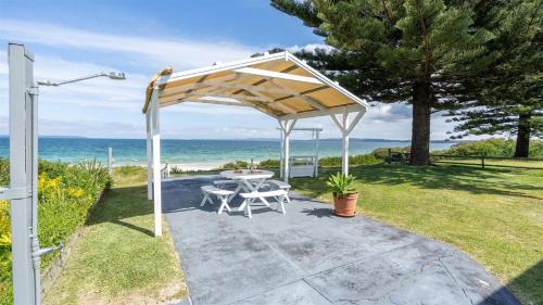 a picnic table under a pavilion with the ocean in the background at Absolute Beach in Callala Beach