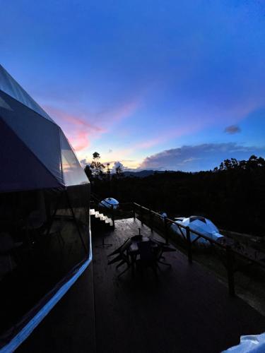 a building with a deck with a sunset in the background at Golden Glamping & Suites in Guatavita