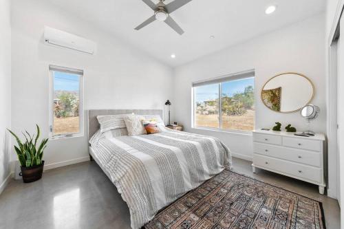 a white bedroom with a bed and a dresser and windows at Whistling Cloud/ Design+Desert Views+National Park in Joshua Tree