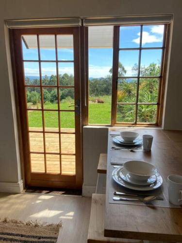 a room with a table with plates and a window at Upmarket off grid cottage on organic farm in secure estate in Howick