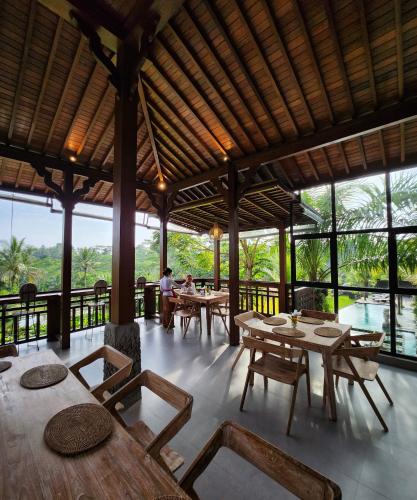 un restaurante con mesas y sillas de madera y ventanas en Pinggala Villa Ubud, en Gianyar