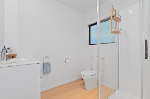 uma casa de banho branca com um chuveiro e um WC. em Tapuaetahi Beach Marvel - Te Tii Holiday Home em Waipapa