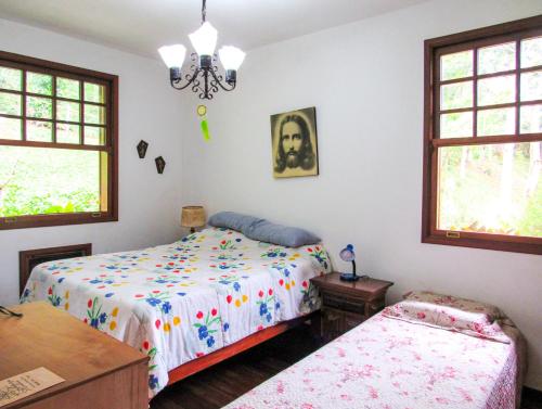 a bedroom with two beds and a table and windows at Casa de campo Hortencia com piscina e lazer - RJ in Teresópolis