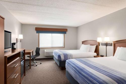 a hotel room with two beds and a desk and a television at AmericInn by Wyndham Sauk Centre in Sauk Centre