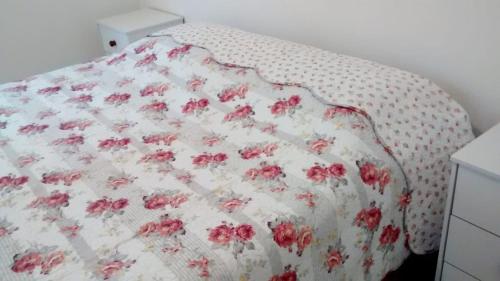 a bed with a white blanket with pink flowers on it at Acomodação corporativa: casa residencial recém-construída in Itatiba
