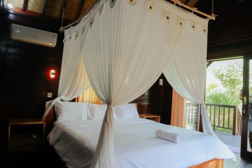 a bedroom with a canopy bed with white sheets and pillows at Mulia Home Stay in Nusa Dua