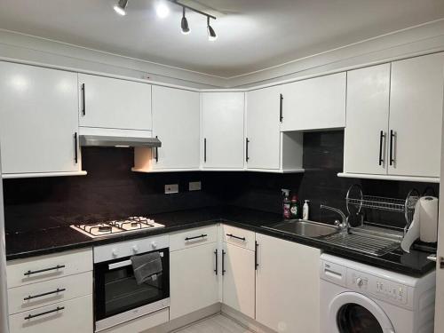 a white kitchen with white cabinets and a sink at Lovely 1-Bedroom Home With Free Parking & Garden. in London