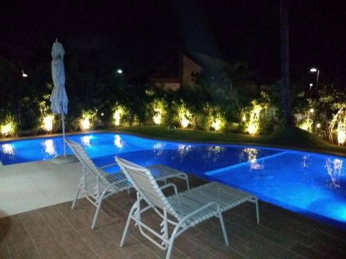 two chairs and a table next to a swimming pool at night at Bangalô Muro Alto Oka Beach Luxo in Porto De Galinhas