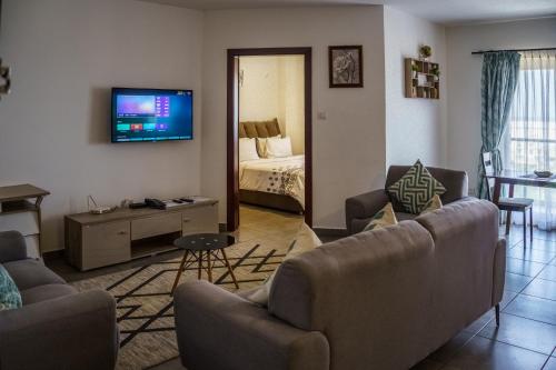 a living room with a couch and a tv on a wall at OASIS PARK RESIDENCE in East Legon