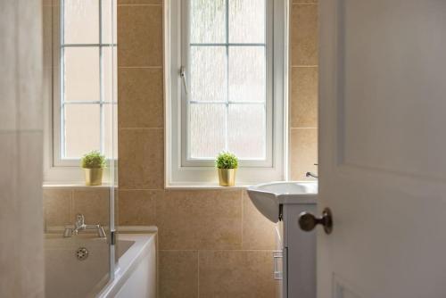 a bathroom with a tub and a sink and two windows at Fairway - modern and stylish holiday home in Kent