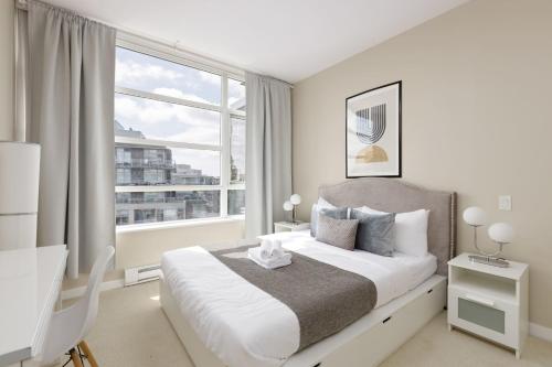 a white bedroom with a bed and a large window at Lovely 2 Bedroom condo with indoor Fireplace for 6 in Burnaby