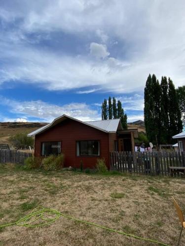 a small red house in a yard with a fence at Cabaña a 8 km de Cerro Castillo. in Villa Cerro Castillo