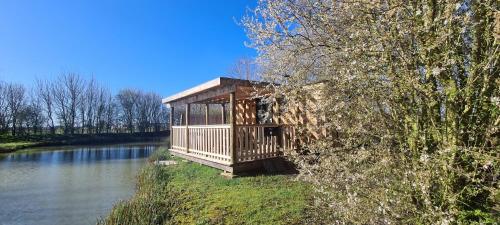 a tree house sitting on the side of a river at Wren - Luxury Shepherd's Hut with Hot Tub in Manea