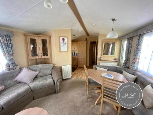 ein Wohnzimmer mit Sofa und Tisch in der Unterkunft Coral Beach - Row 73 Van 2, central heating, WiFi, bed linen - Meadow Lakes Caravan & Lodge Hire in Ingoldmells