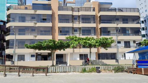 un edificio alto y blanco con árboles delante en Apto pé na areia em Meia Praia Itapema, 3 dormitórios, en Itapema